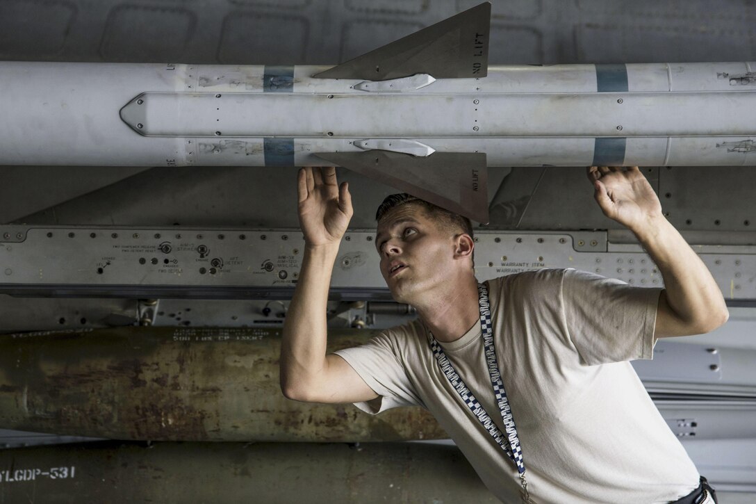 An airman looks up at a missile attached to an aircraft.