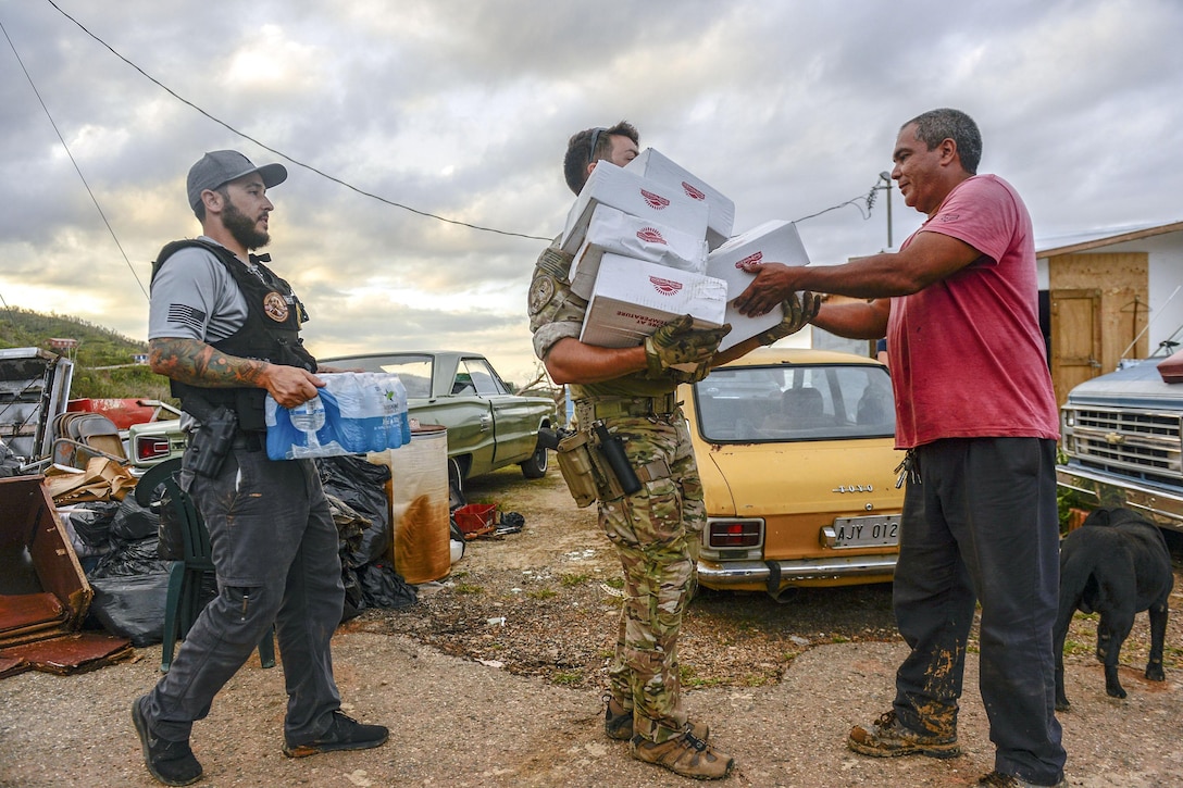 A man passes cardboard boxes to another man, while a third holds a case of water.