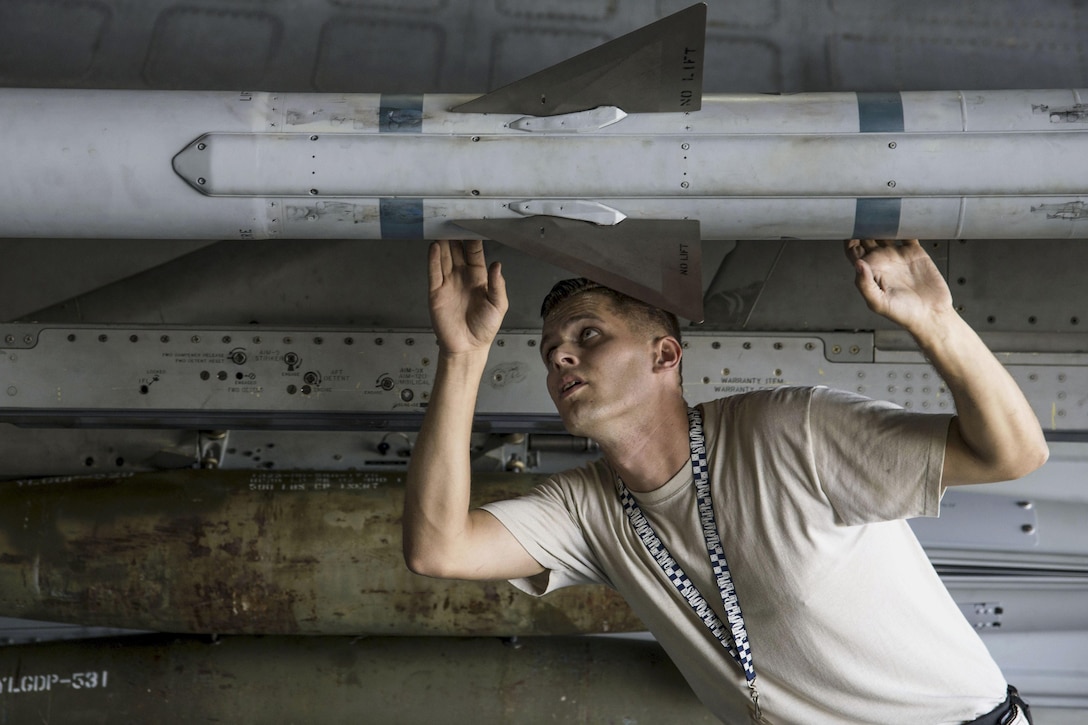 An airman looks up at a missile attached to an aircraft.