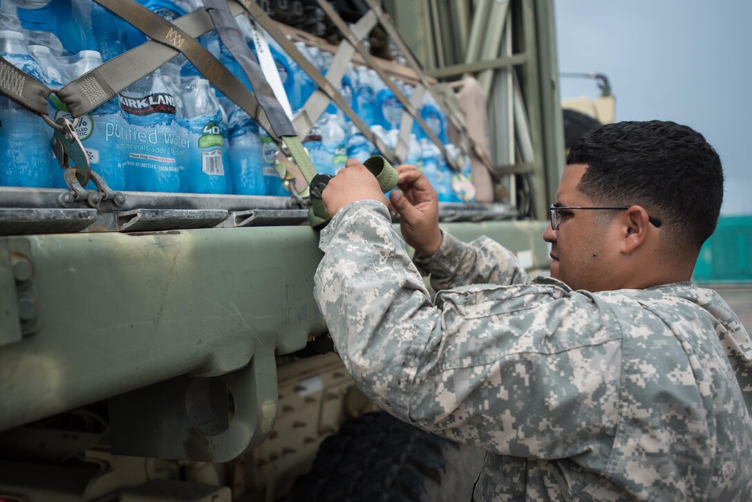 Spc. German Santiago from the Puerto Rico Army National Guard’s 755th Transportation Command straps pallets of water to a flat-bed trailer at Luis Muñoz Marín International Airport in San Juan, Puerto Rico, on Oct. 7, 2017. The cargo will be used for recovery operations following Hurricane Maria. (U.S. Air National Guard photo by Lt. Col. Dale Greer)