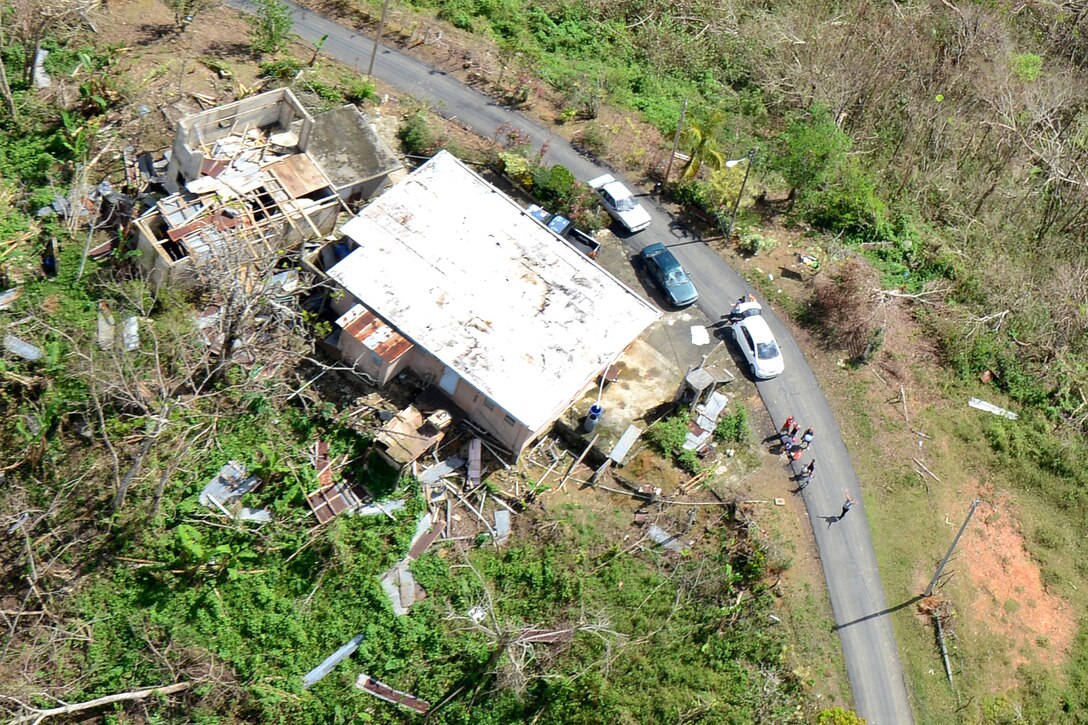 People near a building and debris wave toward a helicopter.