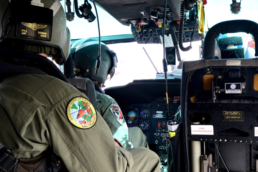 Coast Guardsmen sit behind the controls of a helicopter