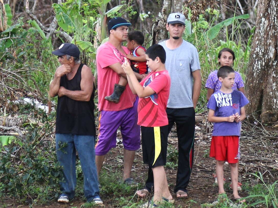 A group of adults and children stand near trees.