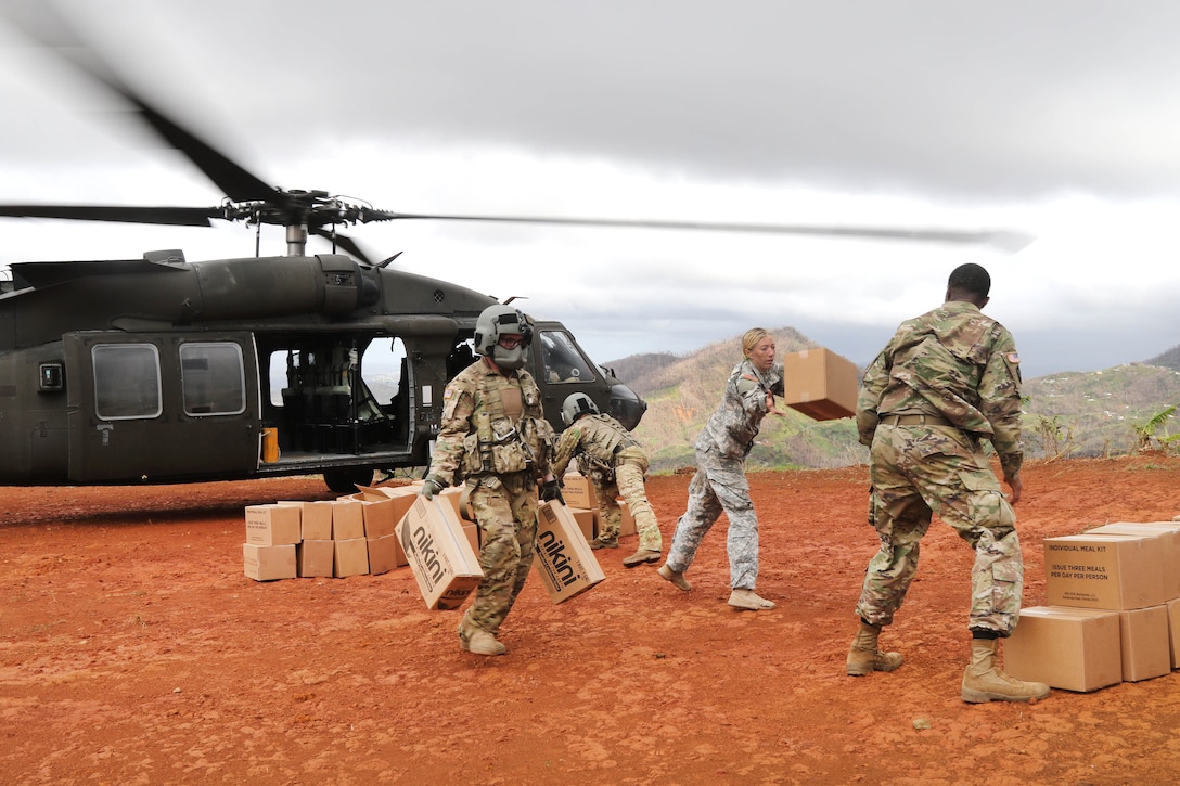 Soldiers move boxes into a pile near a helicopter.