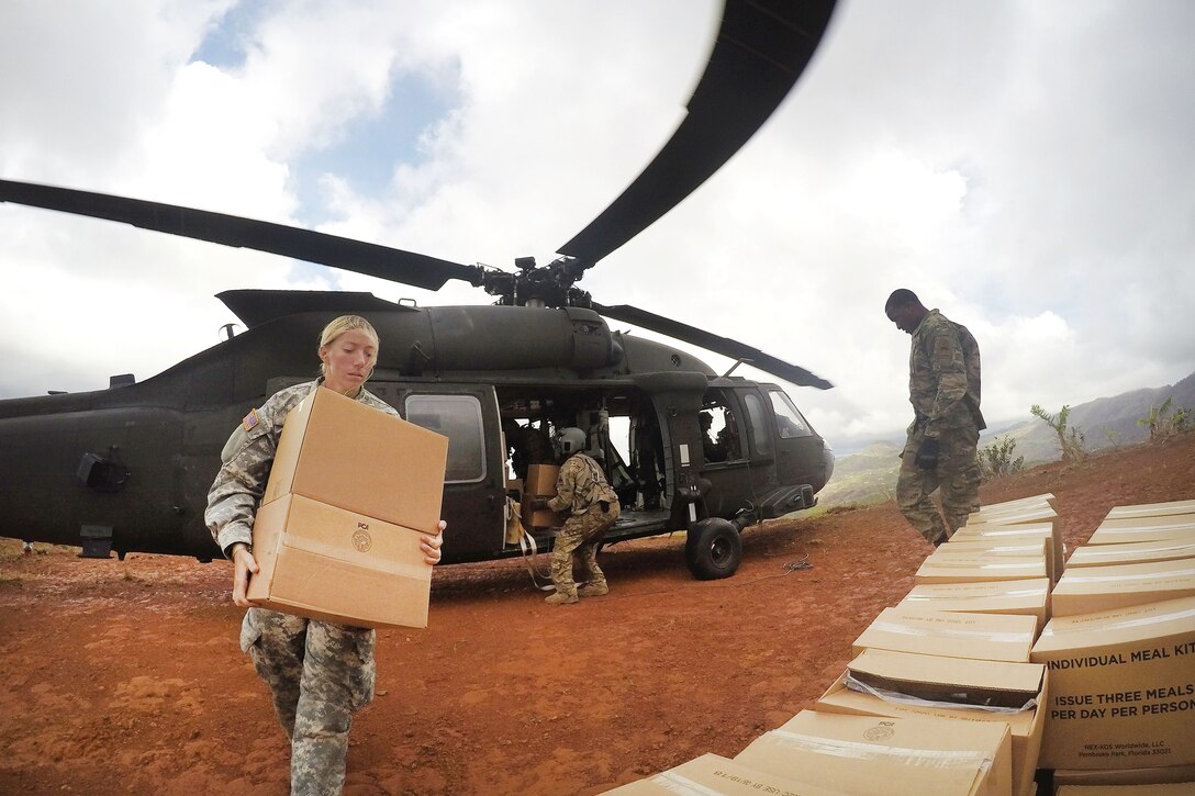 A soldier carries boxes away from a helicopter.