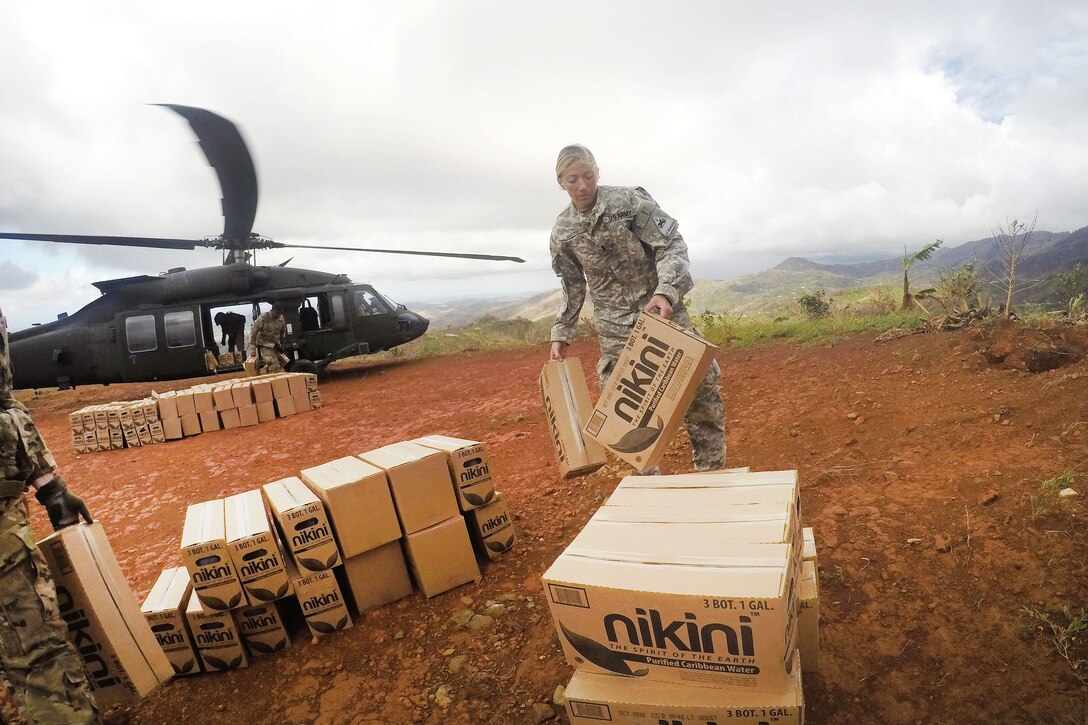 A soldier stacks boxes into a pile near a helicopter.