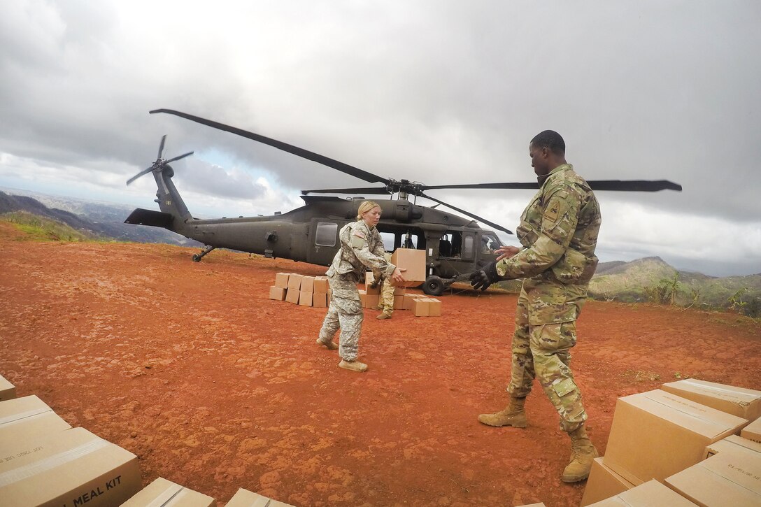 Soldiers unload boxes from a nearby helicopter.