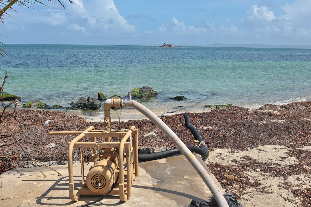 A water pump sits on the beach with hoses running into the water.