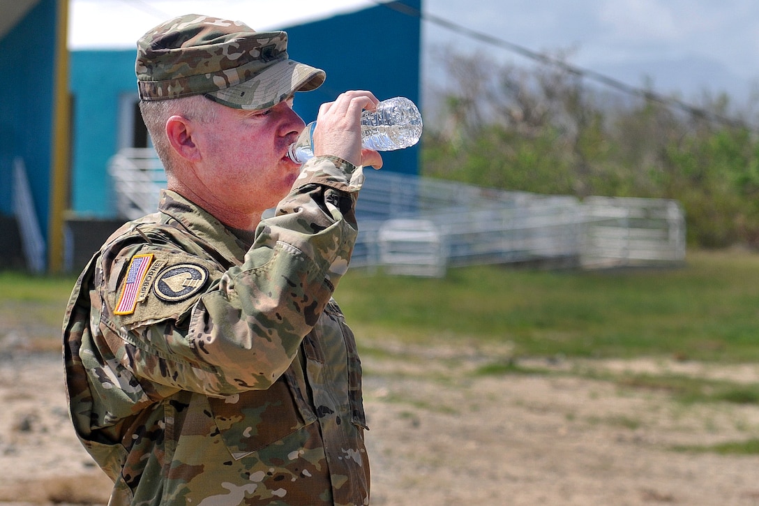 An Army general drinks water from a water bottle.