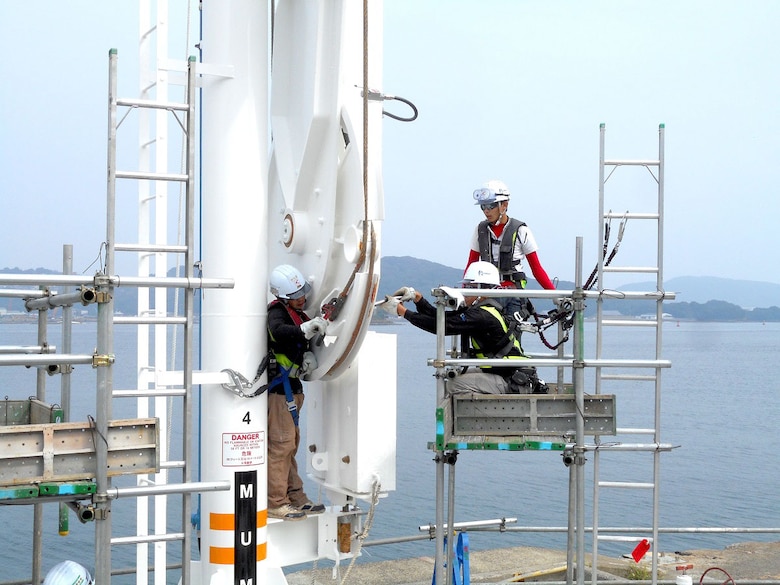 Technicians with Kikkawa, a Japanese contracting company, adjust a wire rope to change the angle of counterweights on one of the newly overhauled marine loading arms at U.S. Fleet Activities Sasebo during final assembly.