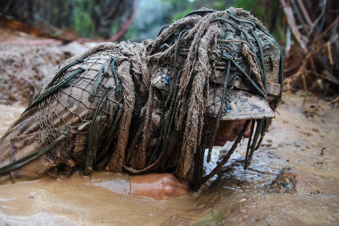 A Marine laying in the mud lifts his head up.
