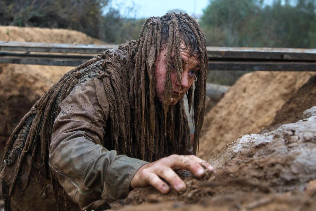 A Marine stands and crawls out of a mud pit while wearing a camouflage suit.