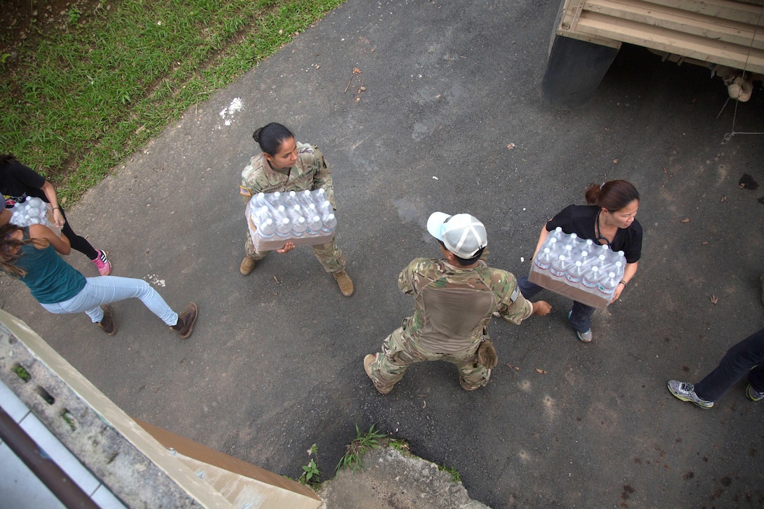 A solders and civilians in a line unload cases of water.