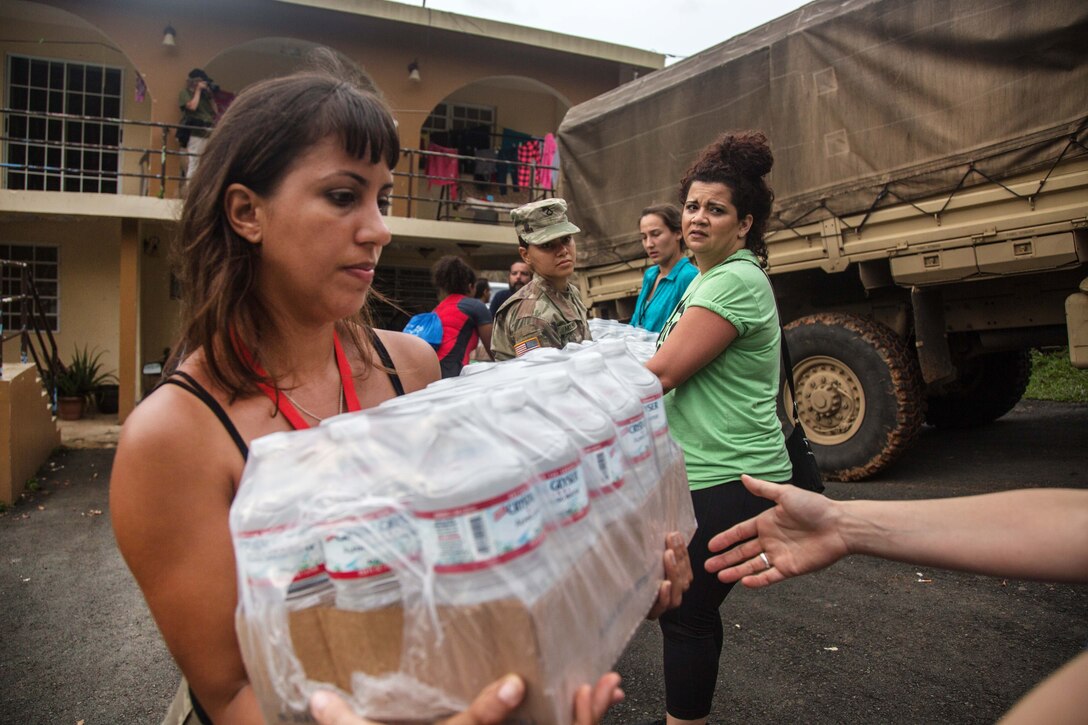 A civilian in a line of people helps unload cases of water.