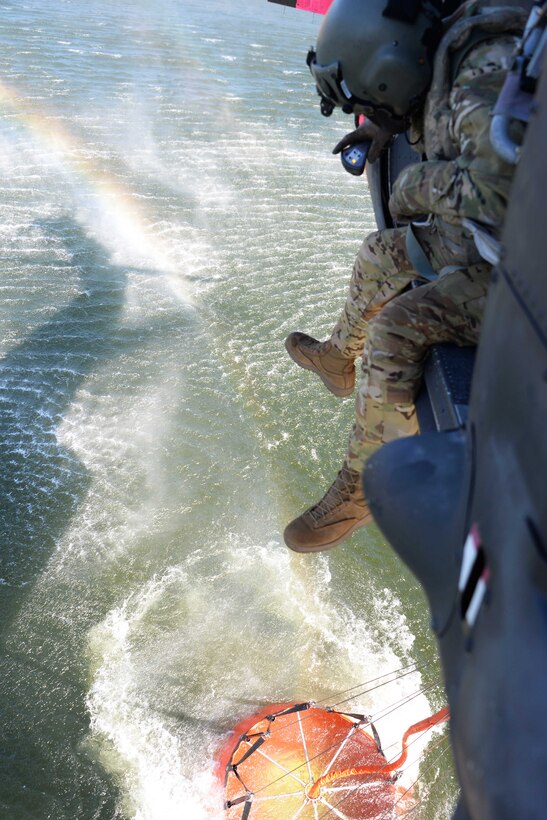 A soldier sits outside a helicopter door over a lake.
