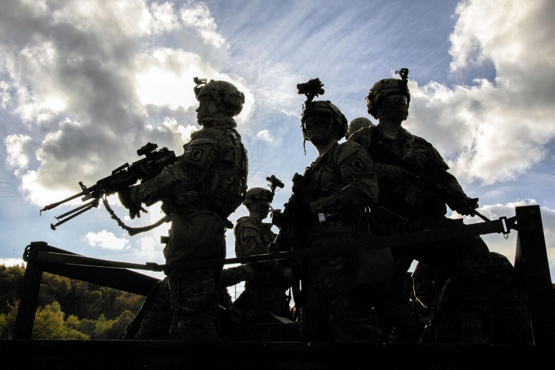 Soldiers, shown in silhouette, stand in a vehicle.
