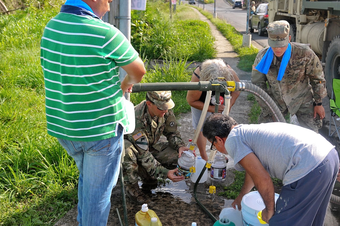 Soldiers and residents gather water from a pipe.