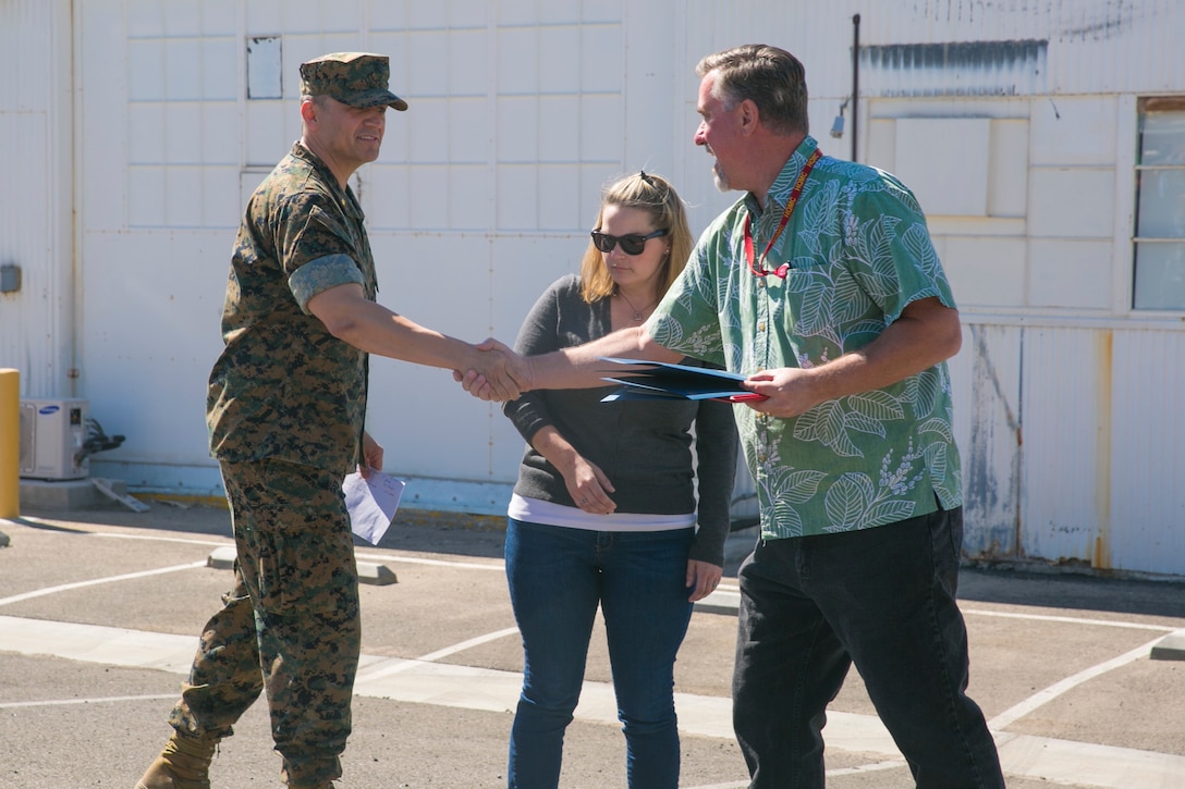 Lt. Cmdr. Juan Chavira, public works officer, Public Works Division, presents time-in-service awards to Glenn Grubbs and Kelley Vendecoevering, workers with PWD, at the PWD Compound aboard the Marine Corps Air Ground Combat Center, Twentynine Palms, Calif., October 10, 2017. Grubbs and Vendecoevering received the awards for dedicating 10 years of service to PWD. (U.S. Marine Corps photo by Lance Cpl. Isaac Cantrell)