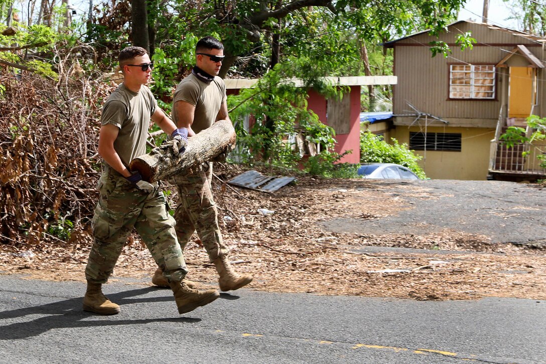 Two Army National Guardsmen carry off a large tree branch.