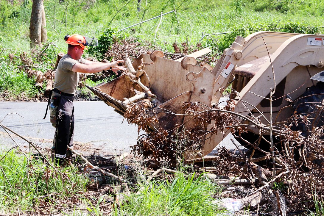 An Army National Guardsman loads branches and debris in the bucket of a backhoe.