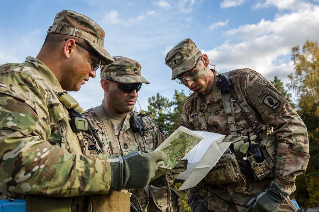 Three soldiers look at a map in paperwork.