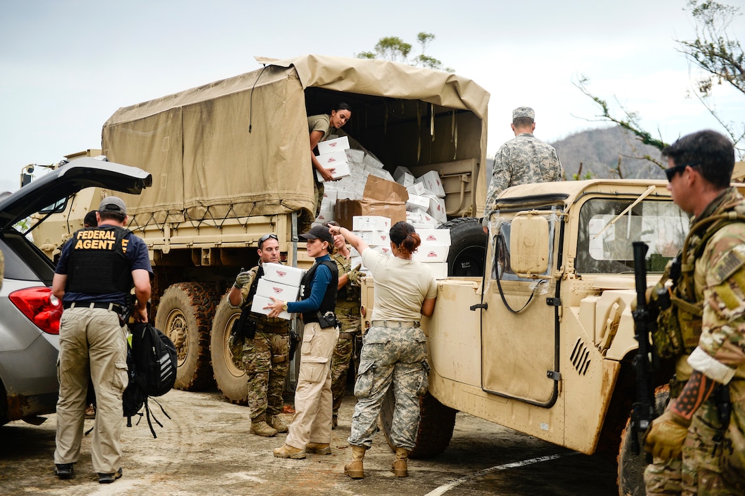 People unload boxes of food out of a military vehicle.