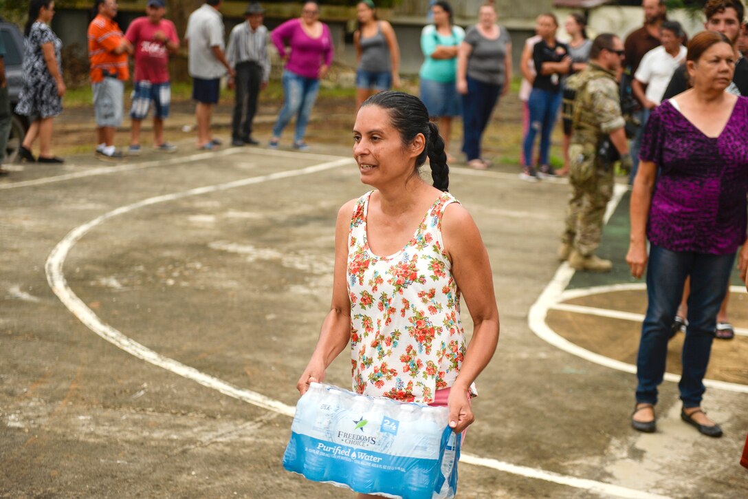 A woman carries a case of water.