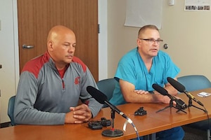 Two men sit at a table with microphones.