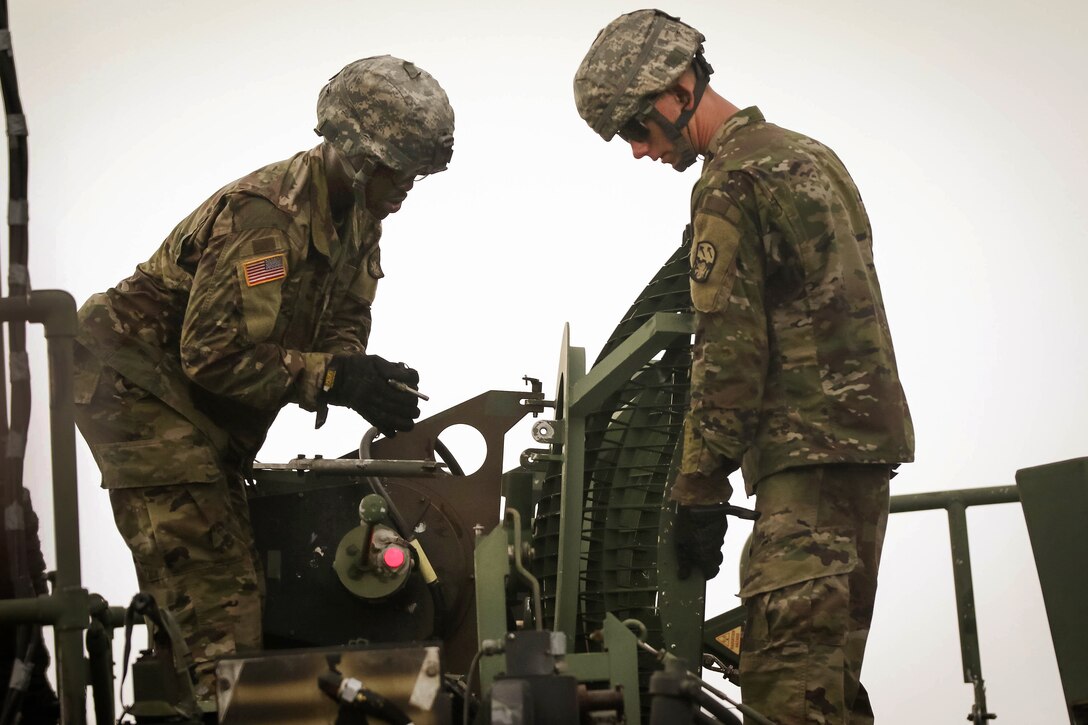 Two soldiers mount an antenna onto a signal tower for a Patriot missile system.