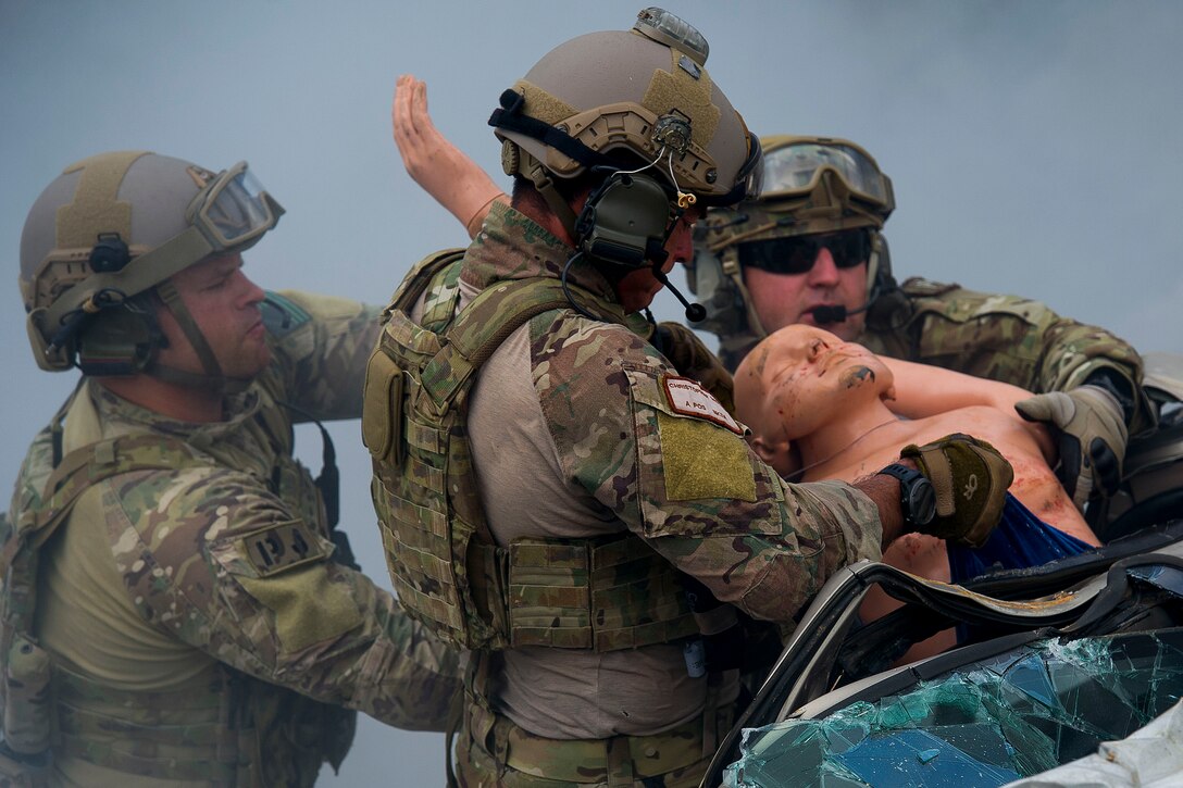 Three airmen remove a dummy from a heavily damaged car.
