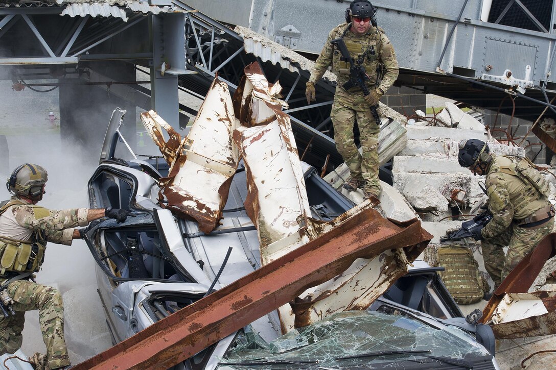 Three airmen look at fallen debris on a crushed car.