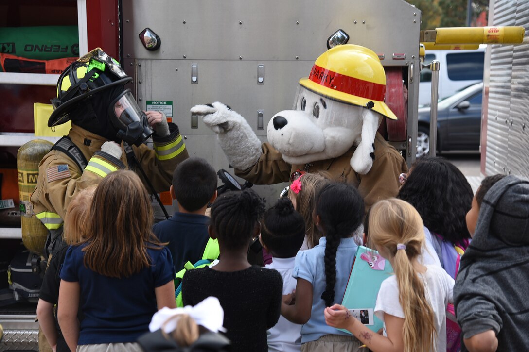 Sparky the mascot, and a 21st Civil Engineer fire fighter talk with children outside the Youth Center on Peterson Air Force Base, Colorado, Oct. 11, 2017. Sparky demonstrated an evacuation with the children during a fire drill. (U.S. Air Force photo by Robb Lingley)