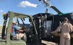 Driver loading items from forklift, left, as other person at right hand-loads items into helicopter