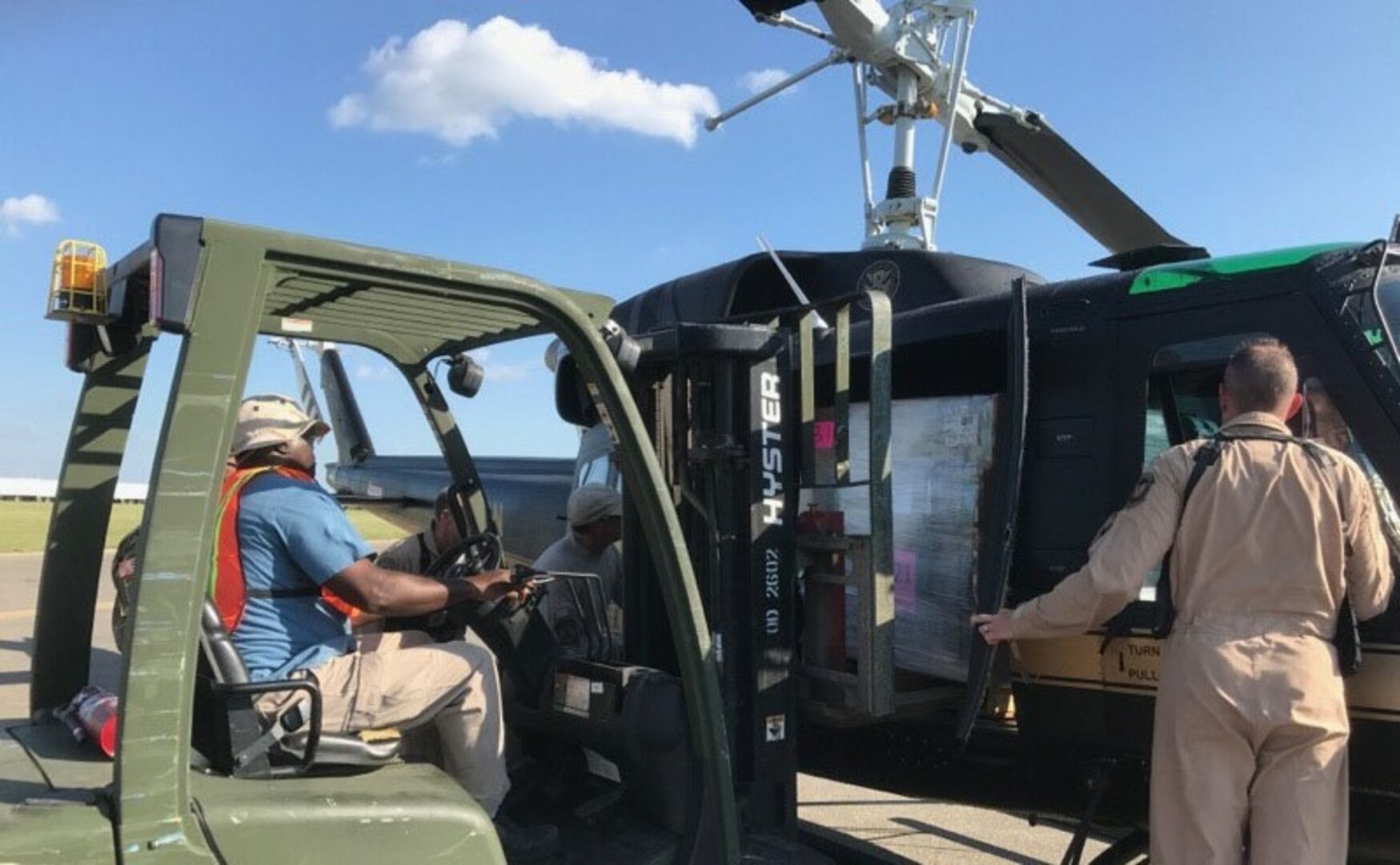 Driver loading items from forklift, left, as other person at right hand-loads items into helicopter