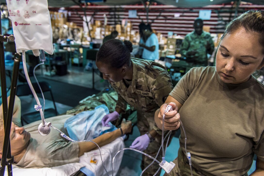 A soldier gives a IV to a commander during training in a hospital.