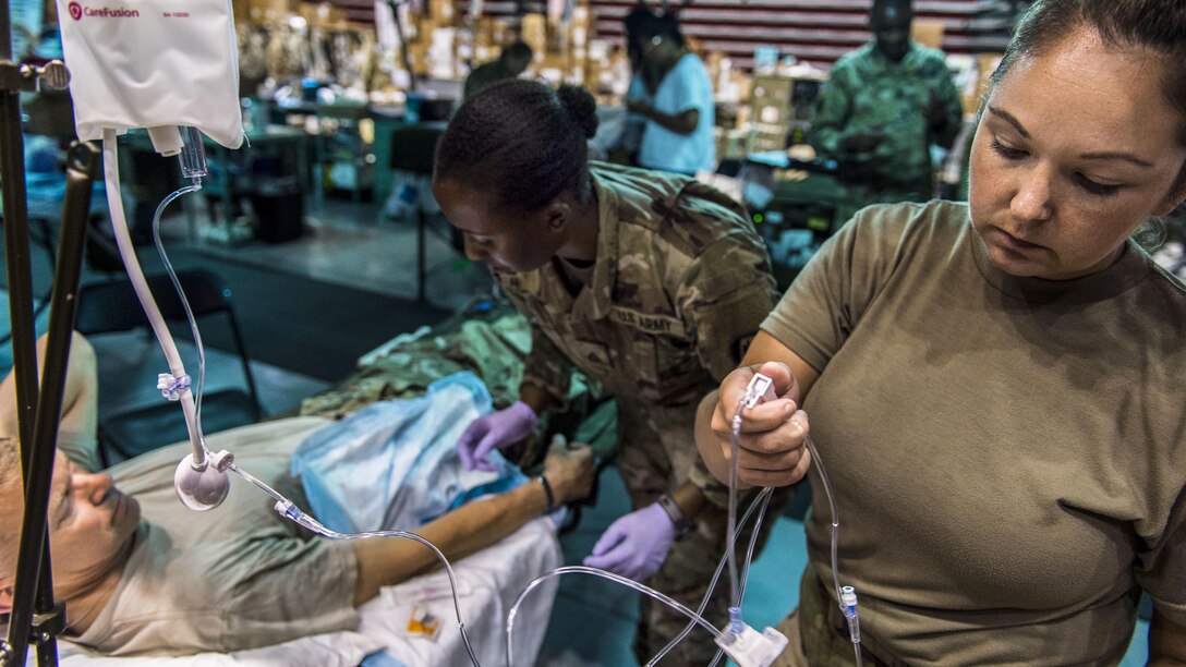 A soldier gives a IV to a commander during training in a hospital.