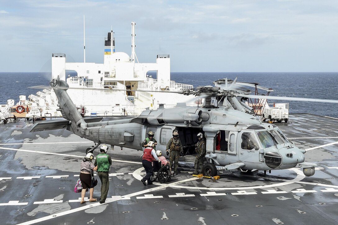 Sailors help load patients from a hospital ship into a helicopter.