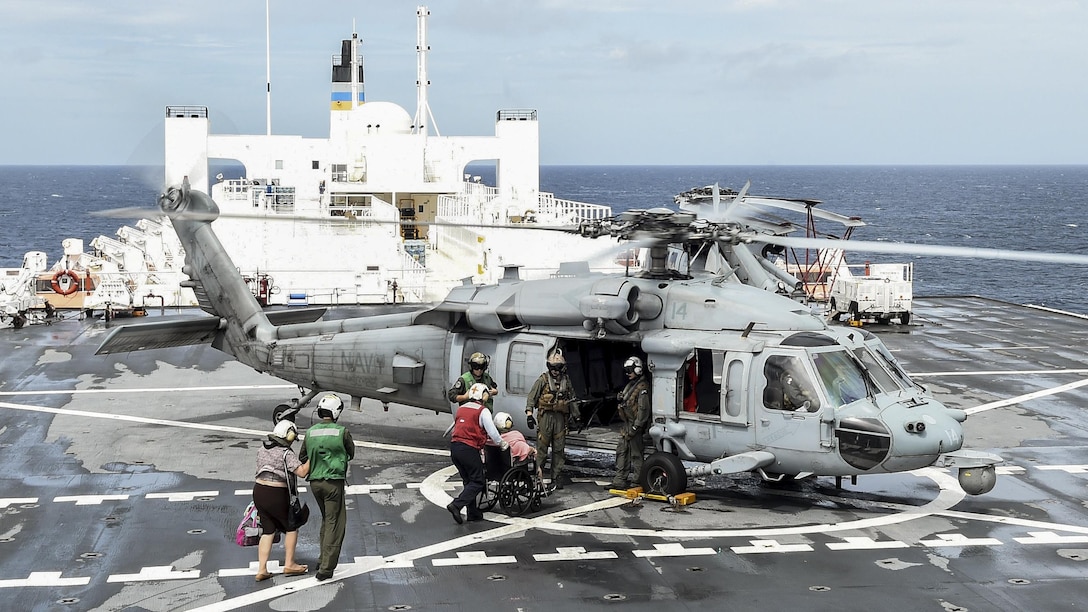 Sailors help load patients from a hospital ship into a helicopter.