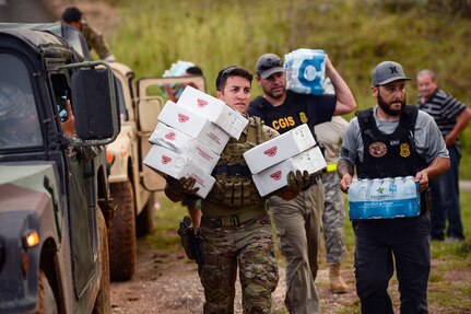 People carry cases of water and boxes of food.