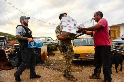 Three people carry boxes of food and a case of water.