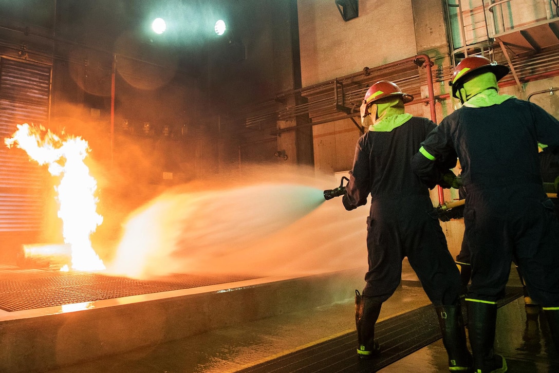 Sailors combat a live fire in the team trainer during a shipboard firefighting course.