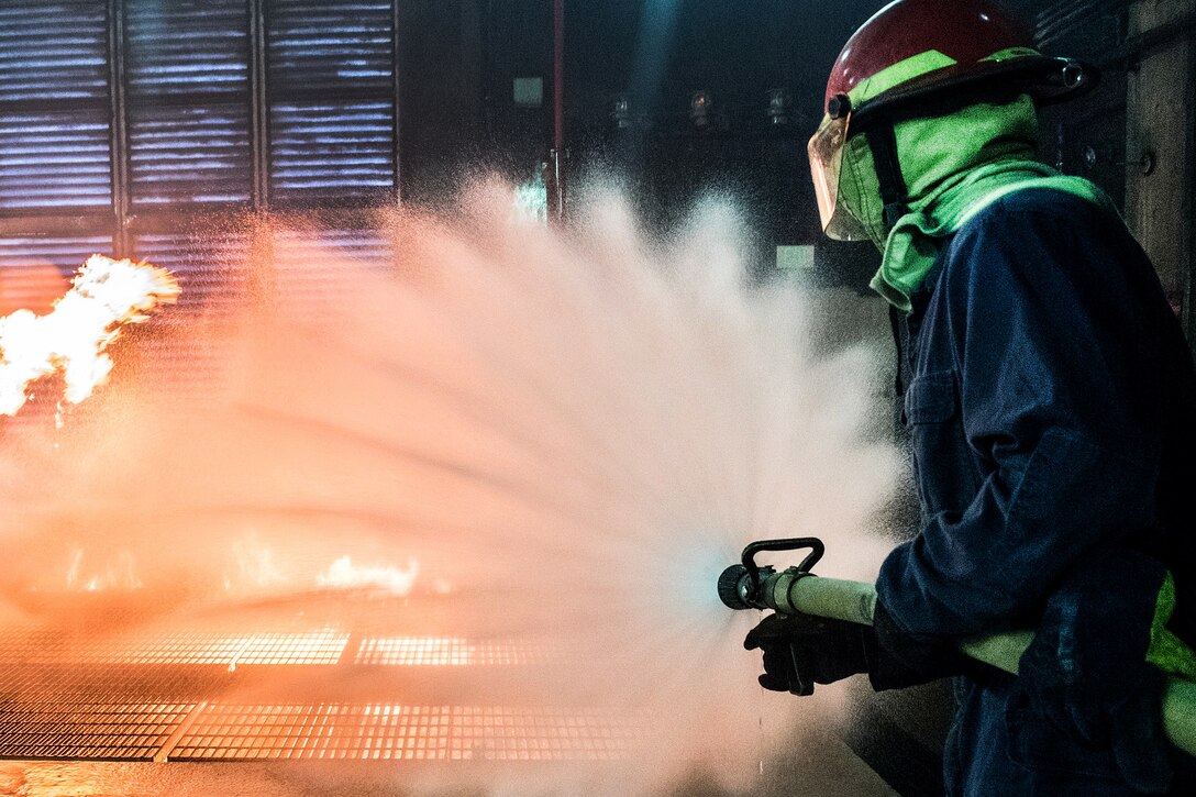 A sailor combats a live fire in the team trainer during a shipboard firefighting course.