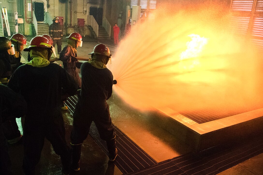 Sailors combat a live fire in the team trainer during a shipboard firefighting course.