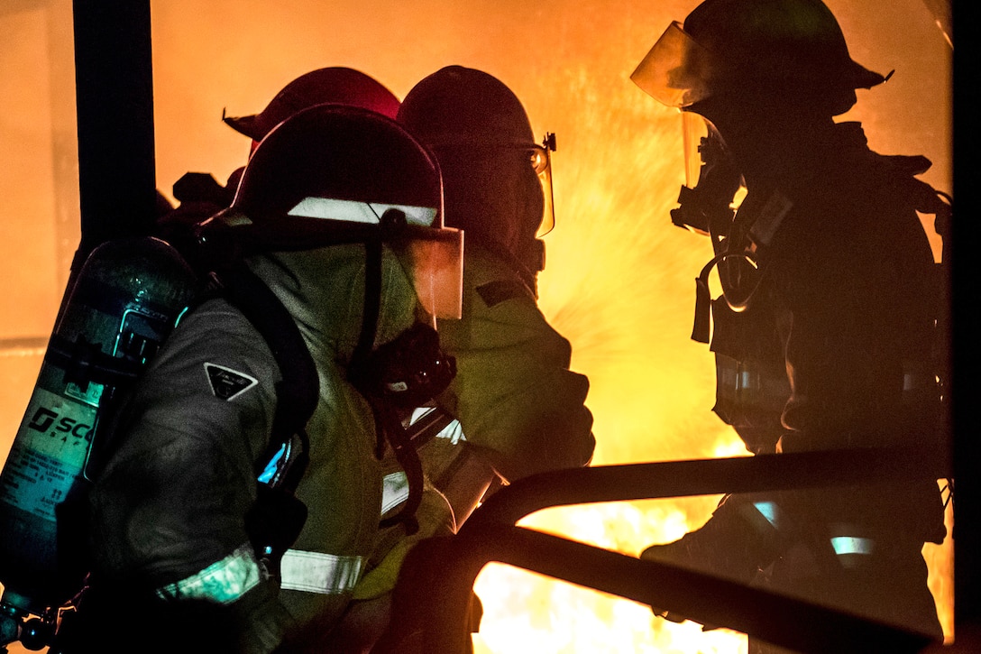 Sailors combat a live fire in the team trainer during a shipboard firefighting course.