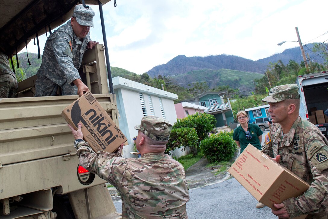 Army Lt. Gen. Jeff Buchanan, right, commander of Joint Task Force Puerto Rico, helps Puerto Rico National Guardsmen unload cases of water and shelf-stable meals.