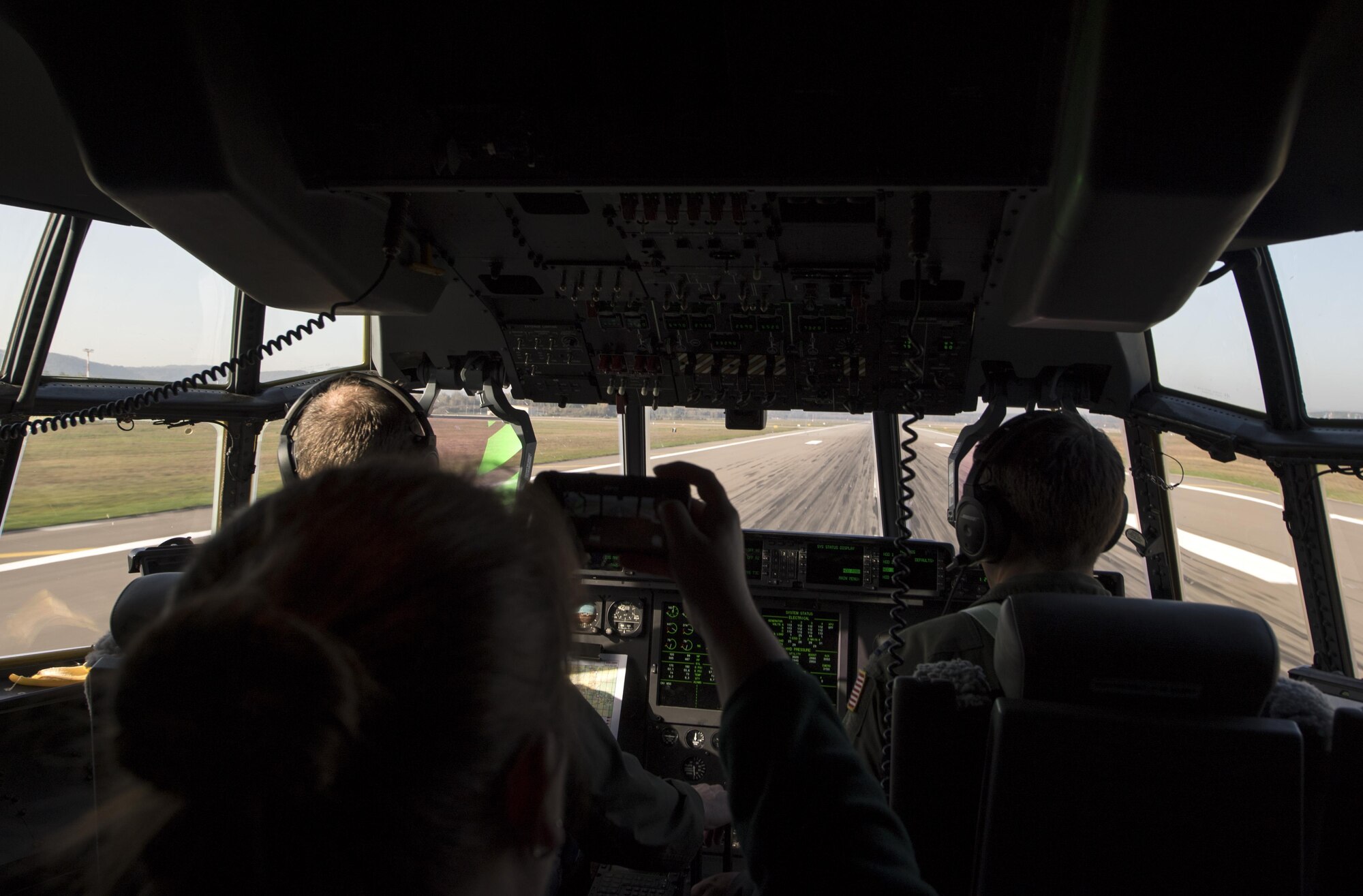 U.S. Air Force Capts. Jared Johnson (left) and Jared Reillings, both 37th Airlift Squadron pilots, land a C-130J Super Hercules while Stefanie Cooper, Ramstein military spouse, films it on her phone at Ramstein Air Base, Germany, Oct. 17, 2017. Cooper, along with other military spouses, flew in the C-130 for the Ramstein Airman and Family Readiness Center’s Heart Link program incentive flight. (U.S. Air Force photo by Senior Airman Tryphena Mayhugh)