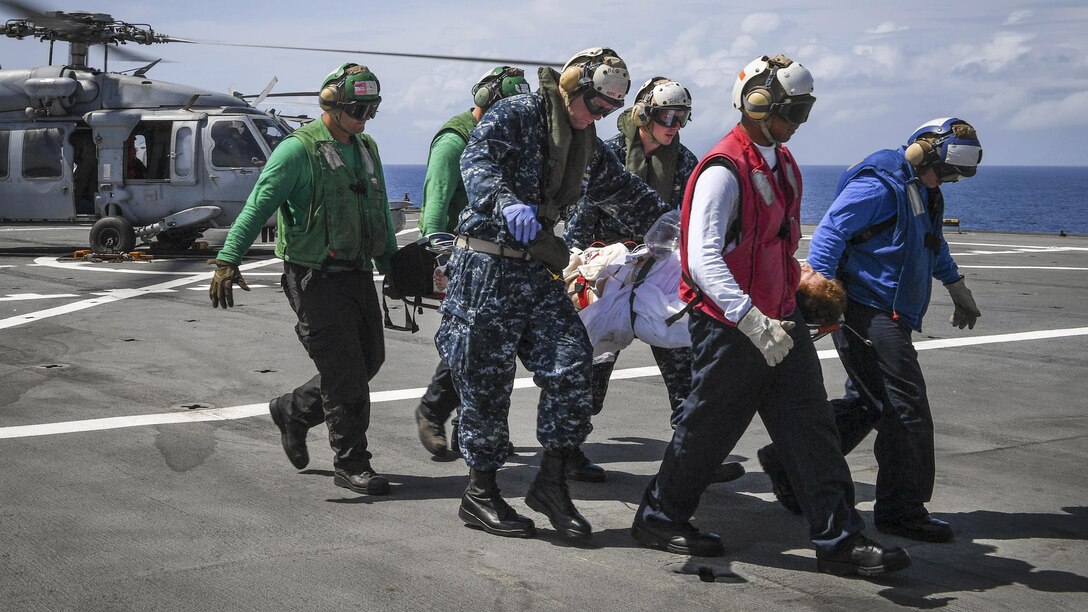 Sailors carry a patient from a helicopter on a military hospital ship.