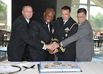 Navy personnel in class A uniforms cutting cake, facing viewer