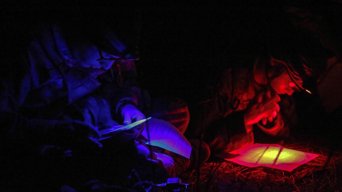Using red and blue lights, two service members look at paperwork.