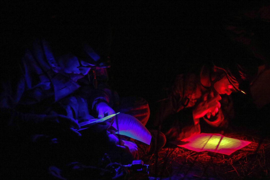 Using red and blue lights, two service members look at paperwork.